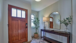 Un pasillo con una puerta de madera, una planta en maceta, una lámpara y una consola.