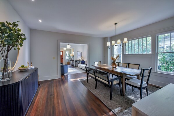 Un comedor moderno con una mesa y sillas de madera, piso de madera oscura y vista a la cocina al fondo.
