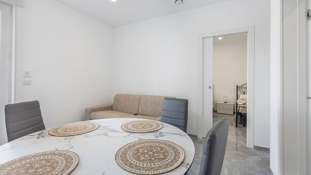A dining area with a round table, two chairs, a sofa, and a bed in the background. - Sole Apartment 1 - Central Marina With Modern Furnishings (Ugento)