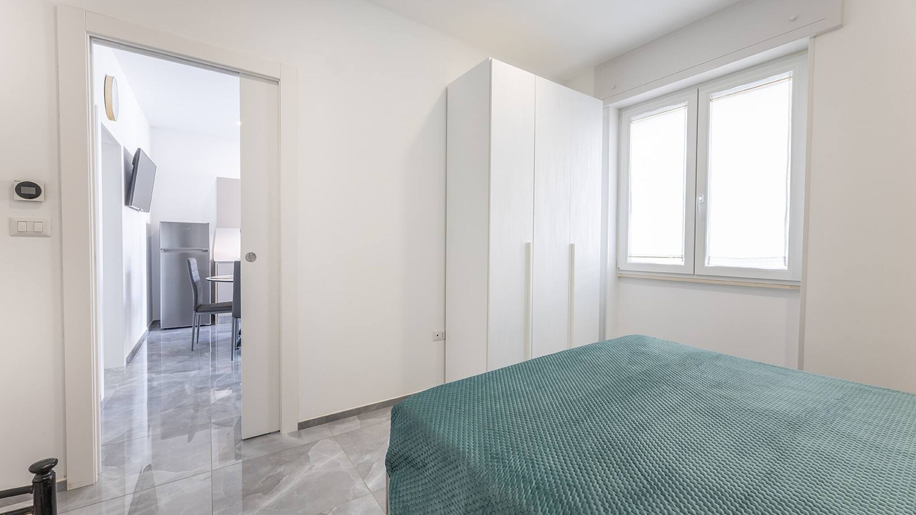 A bedroom with a bed, a window, and a door leading to a bathroom.