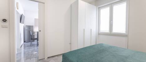 A bedroom with a bed, a window, and a door leading to a bathroom.