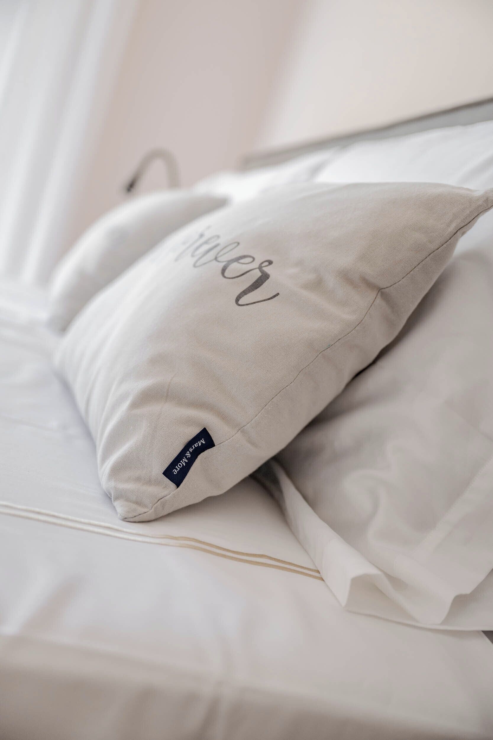 A neatly made bed with white linens and a pillow with the word "Relax" on it.