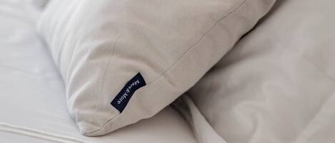 A neatly made bed with white linens and a pillow with the word "Relax" on it.