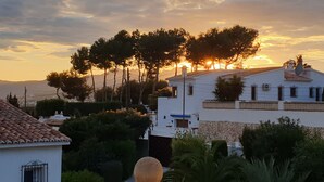 A residential area with white buildings, a stone wall, and a large tree.