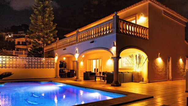 A poolside area with a pool, seating, and a building with arched doorways and columns.