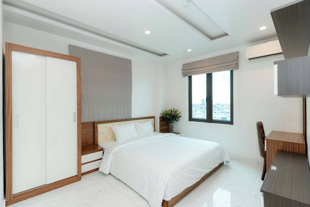 A modern bedroom with a bed, a wardrobe, a desk, and a window with a city view.