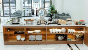 A buffet setup with various dishes and utensils, a coffee station, and a seating area with a sofa and chairs.