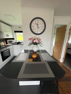 A modern kitchen with white cabinets, a microwave, a stove, and a dining area with a black table and a clock on the wall.