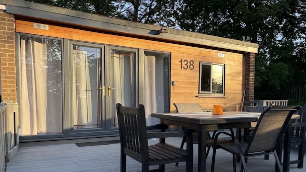 A wooden building with the number 138, a patio with a table and chairs, and a sliding glass door. - Beautiful Snowdonia Tree Top View Chalet in North Wales (Caeathro)