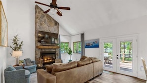 A living room with a stone fireplace, a ceiling fan, a large sofa, and a view through glass doors to an outdoor area. - The Greatest Cove, Man! | Spectacular Panoramic Playground (Henrico)