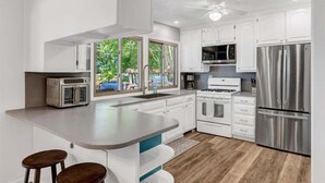 A modern kitchen with white cabinets, stainless steel appliances, a central island with stools, and large windows. - The Greatest Cove, Man! | Spectacular Panoramic Playground (Henrico)