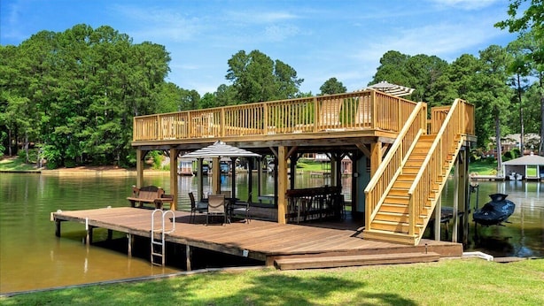 A wooden deck with a covered seating area, a staircase, and a view of a lake. - The Greatest Cove, Man! | Spectacular Panoramic Playground (Henrico)