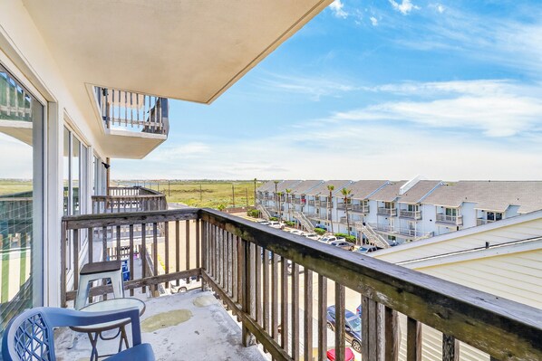 A balcony with a view of a row of buildings, a wooden railing, and a clear sky.