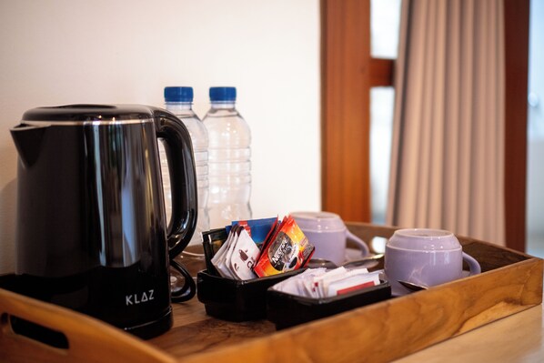 A tray with a black coffee maker, two water bottles, a coffee pod, a tea bag, and a purple cup.