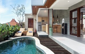 A modern outdoor pool area with lounge chairs, a kitchen, and a dining area.