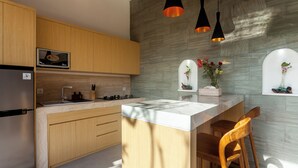 A modern kitchen with wooden cabinets, a stainless steel refrigerator, a built-in oven, and a central island with a bar stool. - Green Kulu Villa (Tampaksiring)