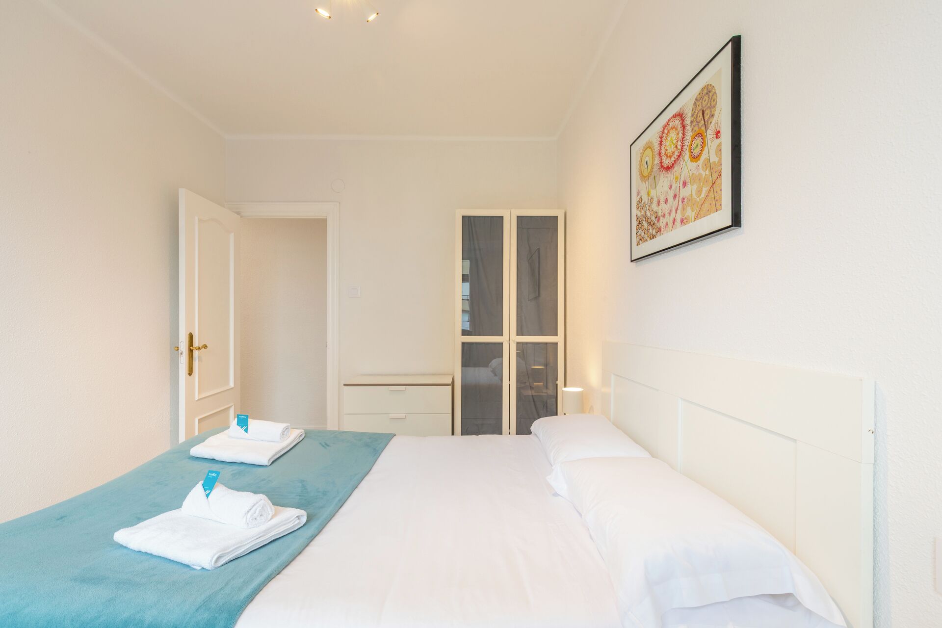 A hotel room with a bed, a blue accent wall, a wardrobe, and a framed artwork on the wall.