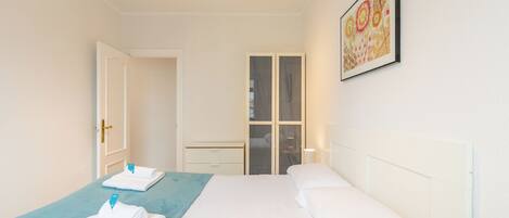 A hotel room with a bed, a blue accent wall, a wardrobe, and a framed artwork on the wall.