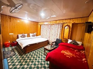 Una habitación con paredes de madera, una cama con ropa blanca, un sofá rojo, una mesita con una lámpara y un suelo estampado.