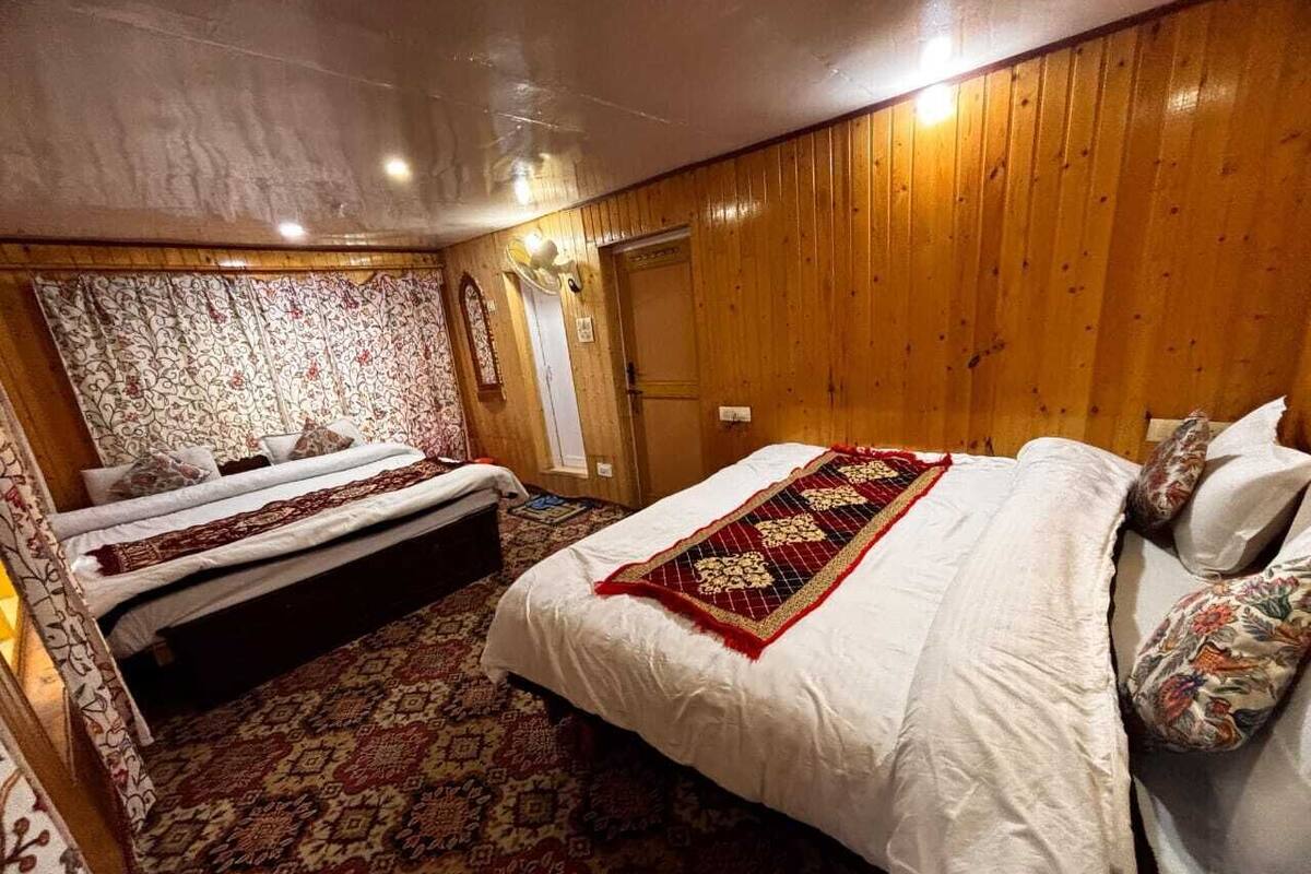A room with two beds, a patterned carpet, wooden walls, and a door.