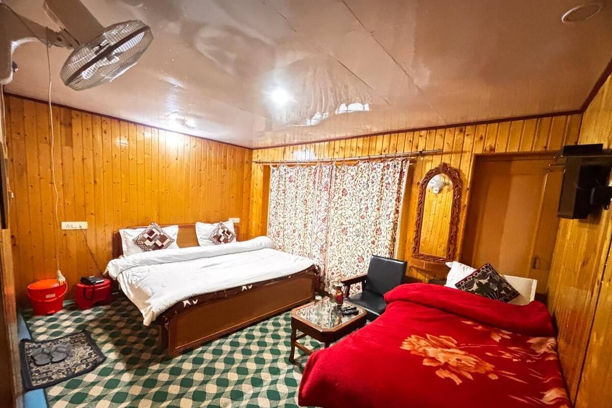 A room with a bed, a desk, a chair, a fan, and a red blanket.