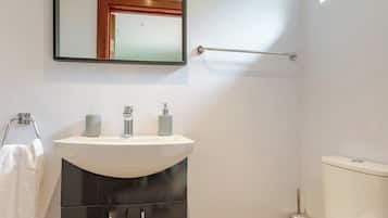 A compact bathroom with a white sink, a black cabinet, a white toilet, and a mirror above the sink.
