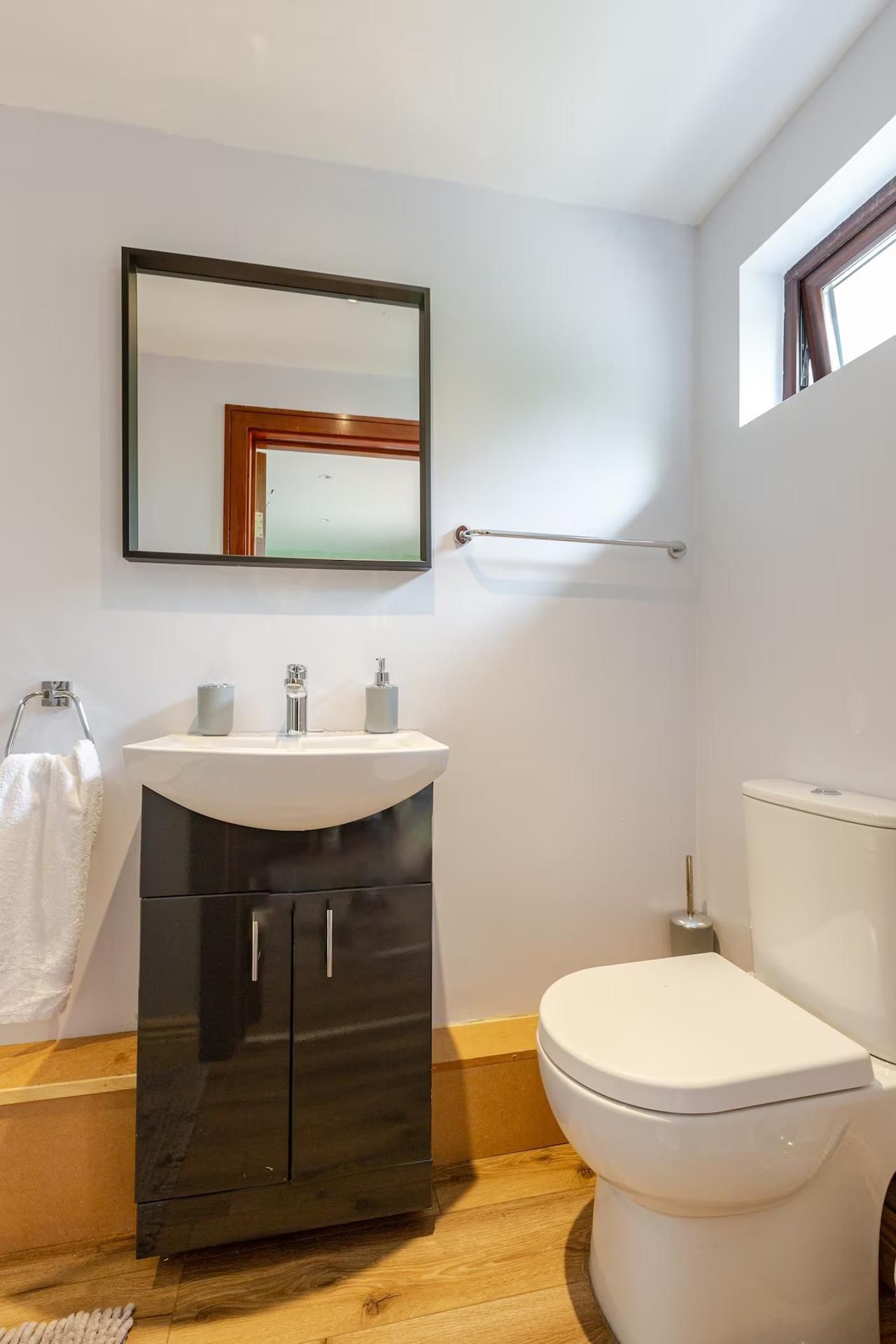 A compact bathroom with a white sink, black cabinet, and a white toilet.