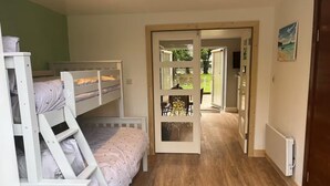 Una habitación con literas, piso de madera, una puerta que da a un jardín y un cuadro en la pared.