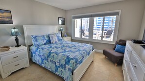 A bedroom with a bed, bedside tables, a dresser, a window with a view of buildings, and a painting on the wall.