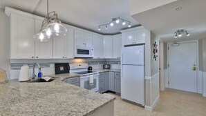 A modern kitchen with white cabinets, granite countertops, a built-in microwave, a stove, a refrigerator, and pendant lighting.