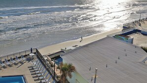A beachside view with a pool area, beach rentals sign, and a person walking on the beach.