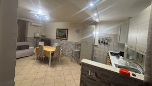A compact kitchen with a dining area, a sofa, and a painting on the wall.
