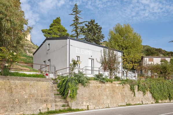 Un bâtiment dont la façade porte l’inscription « ELCHIMA », entouré de verdure et délimité par un mur de pierres.