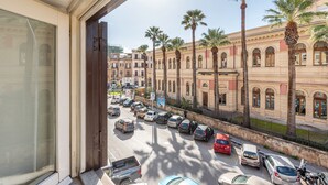 A view from a window overlooking a street with parked cars and palm trees, with buildings in the background. - Kadì Apartment by Wonderful Italy (Palermo)
