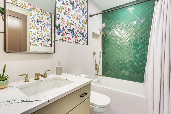 Un baño con lavamanos blanco, inodoro, bañera y ducha con revestimiento de azulejos tipo espiga verde.