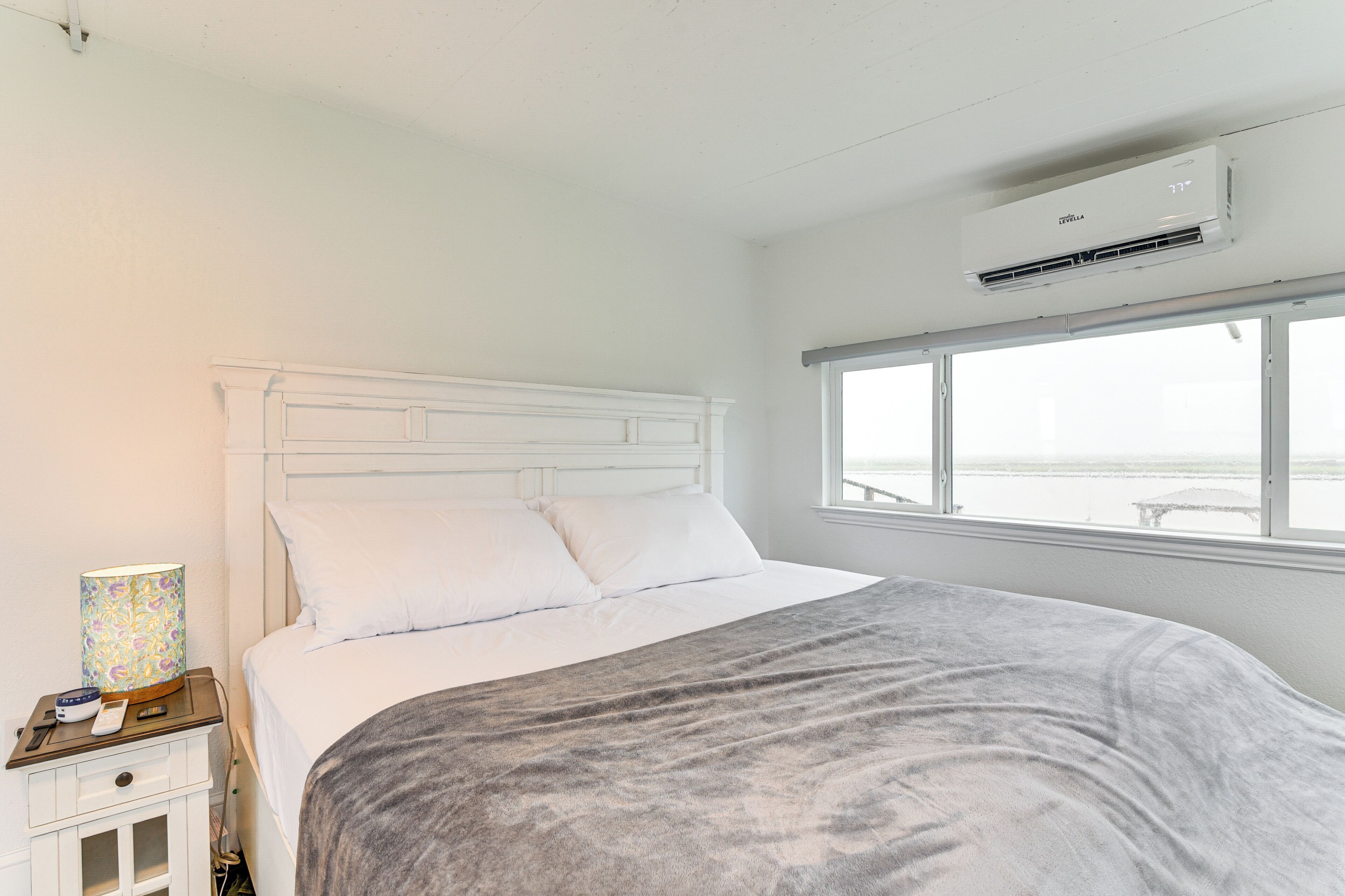 Un dormitorio con cama, mesita de noche, lámpara y ventana con vistas.
