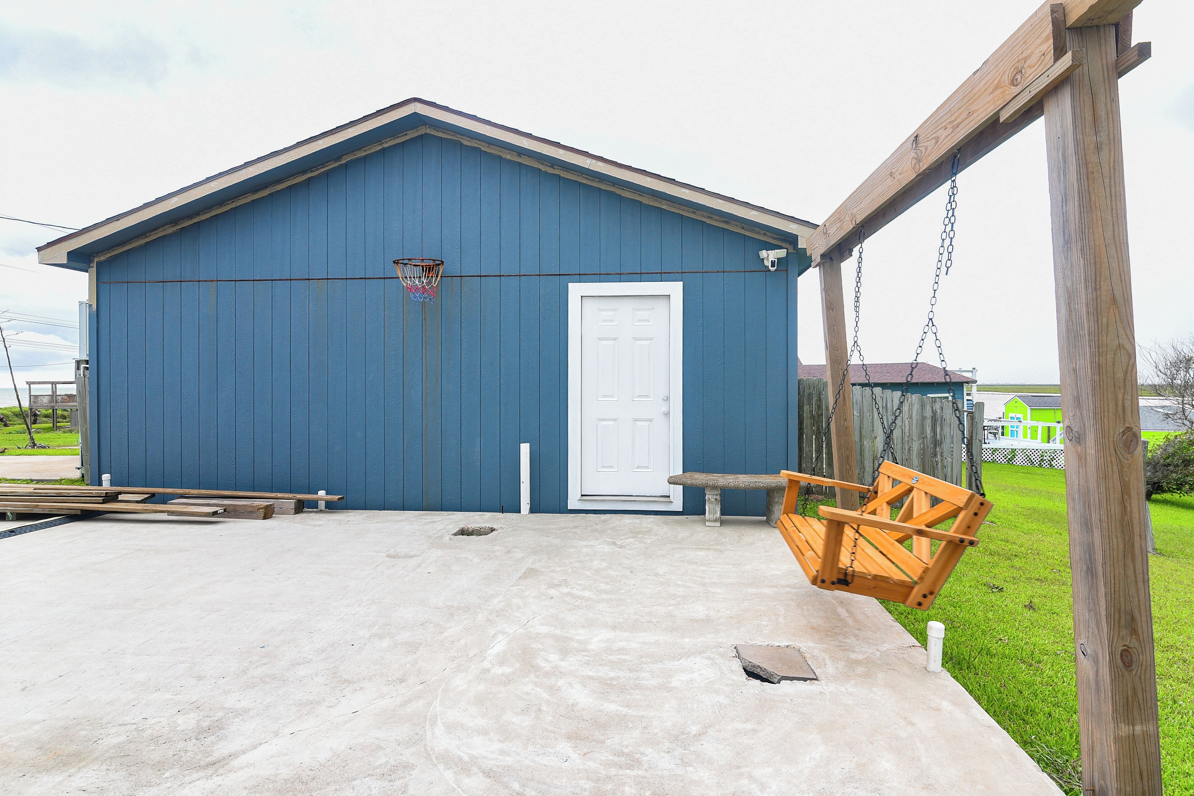 A blue building with a white door, a concrete patio, and a wooden swing set.