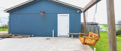 A blue building with a white door, a concrete patio, and a wooden swing set.