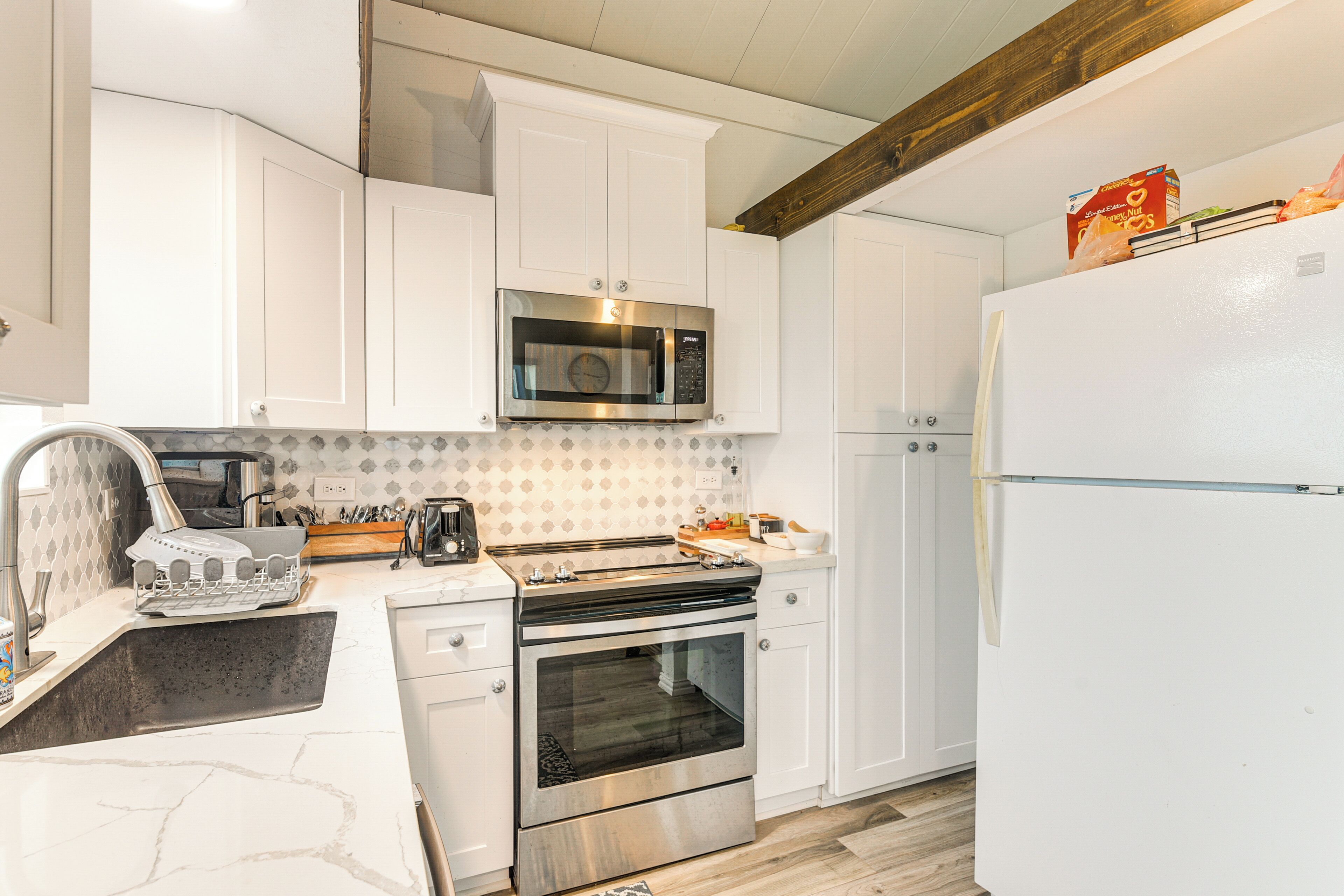 A modern kitchen with white cabinets, a stainless steel microwave, an oven, and a refrigerator.