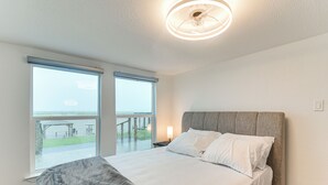 Une chambre à coucher comprenant un lit, une table de chevet, une lampe et une vue sur l’extérieur grâce à de grandes fenêtres.
