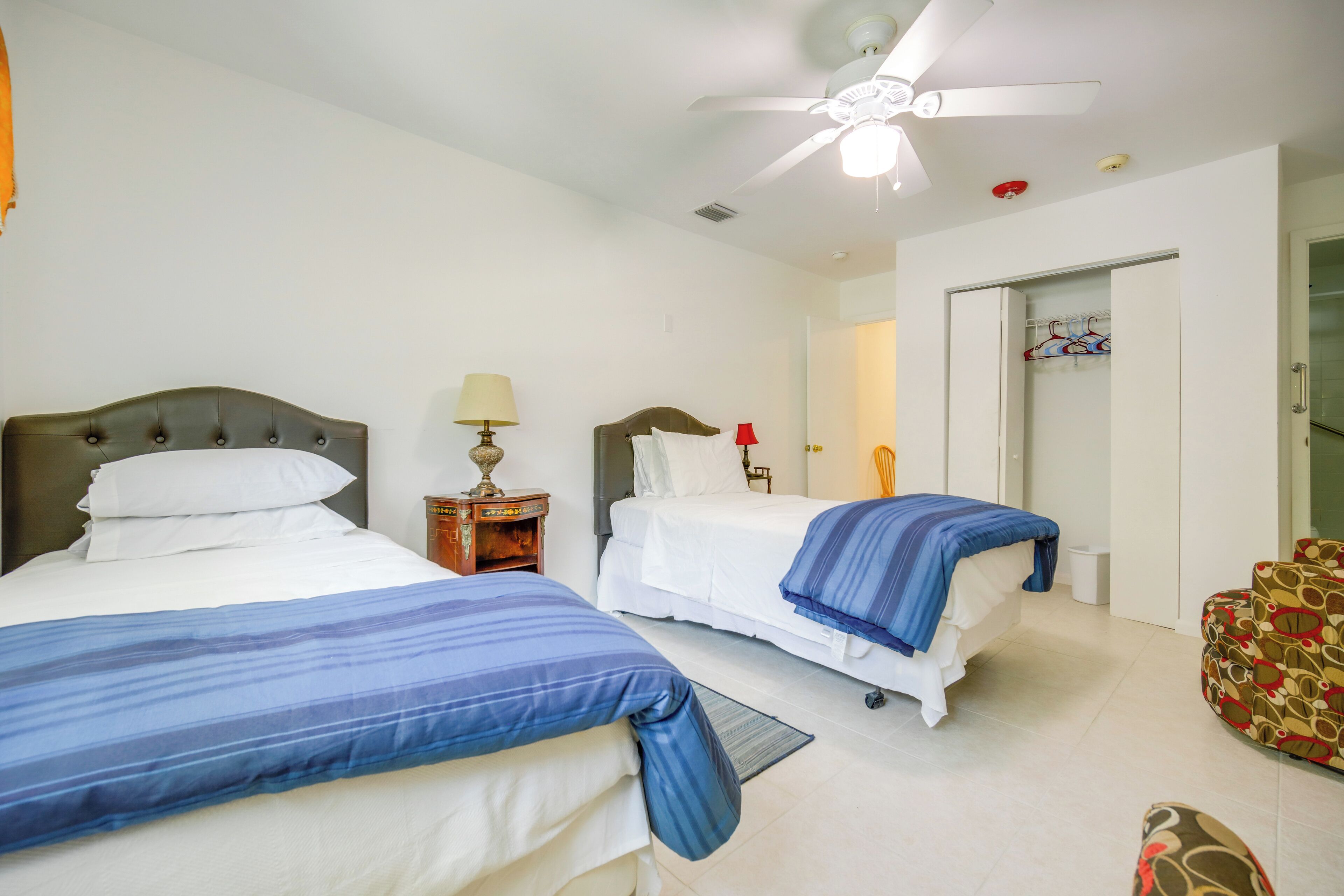 A hotel room with two beds, a ceiling fan, a wardrobe, and a chair.