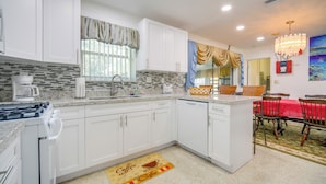 A modern kitchen with white cabinets, a coffee maker, and a dining area with a red tablecloth. - < 3 Mi to Hard Rock Stadium: Miami Home w/ Sunroom (Miami Gardens)