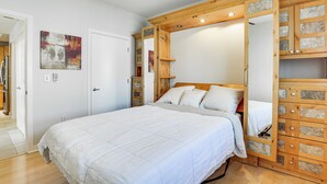 Un dormitorio con una cama grande, un armario de madera con cajones, un ventilador de techo y una puerta que da a otra habitación.