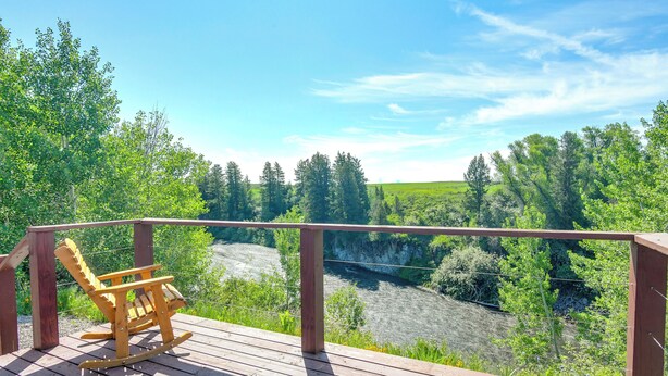 A wooden deck with a rocking chair overlooking a river and forested area. - Teton Mtn Views: Peaceful Riverfront Cabin! (Ashton)
