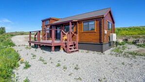 A log cabin with a porch, a gravel driveway, and a clear blue sky. - Teton Mtn Views: Peaceful Riverfront Cabin! (Ashton)