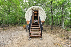 Una estructura de madera cubierta con una escalera que conduce a una entrada, rodeada por un bosque.