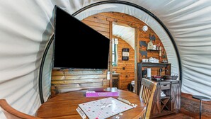 A cozy interior of a tent with a wooden table, chairs, a Scrabble game, and a television. - Covered Wagon Vacation Rental in Broken Bow! (Broken Bow)