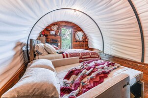 Un acogedor espacio tipo tienda con forma circular, que incluye una cama, almohadas, una colcha, una pared de madera con un espejo y un cartel.