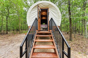 Una tienda de campaña con una escalera de madera que lleva a una cama en su interior, rodeada por un bosque.