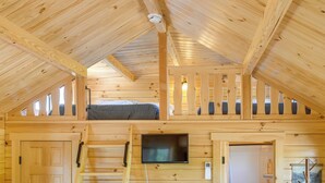 Una cabaña de madera con habitación en la buhardilla, un televisor montado en la pared y una escalera que lleva al camarote superior.